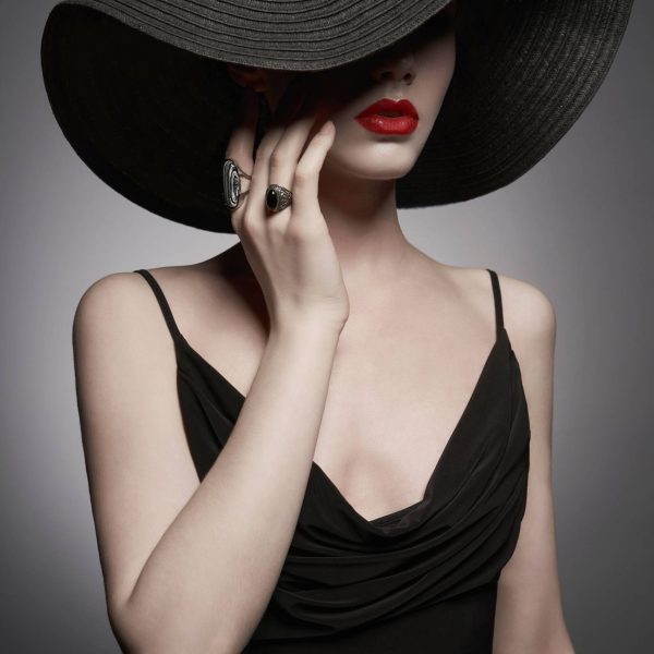 portrait of young lady with black hat and evening dress Fashion portrait of young sexy lady with beautiful black hat and evening dress. Stylish elegant woman with modern jewelry. Studio photo of pretty model on grey background.