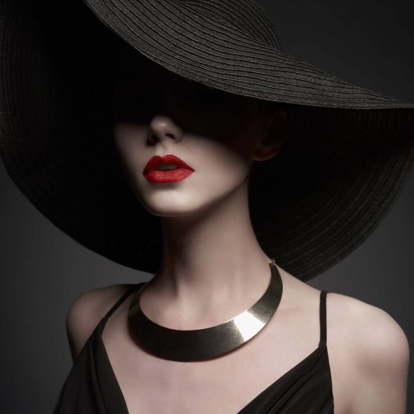 portrait of young lady with black hat and evening dress Fashion portrait of young sexy lady with beautiful black hat and evening dress. Stylish elegant woman with modern jewelry. Studio photo of pretty model on grey background.